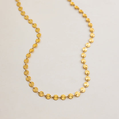 Flat lay of gold sunburst disc choker necklace with textured circular links