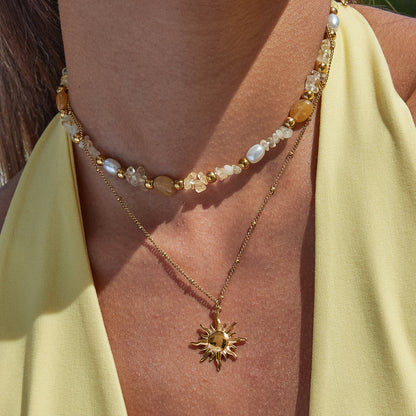 Gold necklace with sun pendant worn by a person in a yellow top.