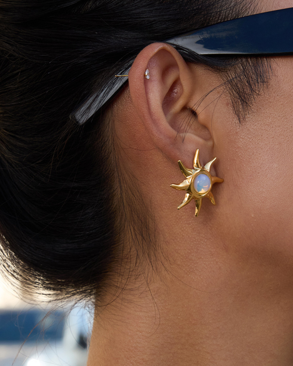 Gold sun-shaped earring with a central gemstone worn by a person.
