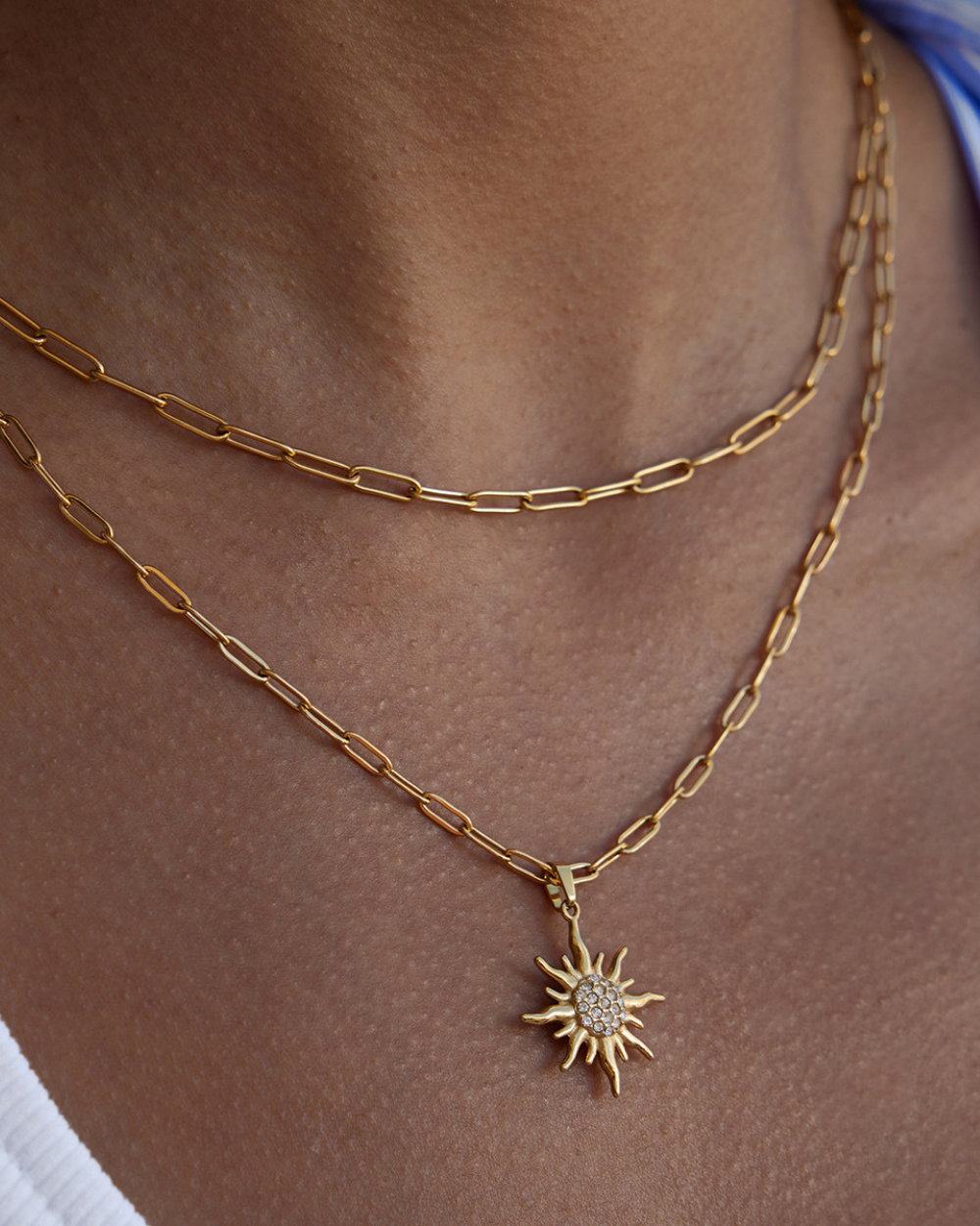 Gold chain necklace with a sun-shaped pendant on a person's neck.