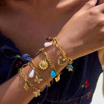Gold layered bracelet set with sunflower and turquoise charms, worn on tanned wrist at the beach