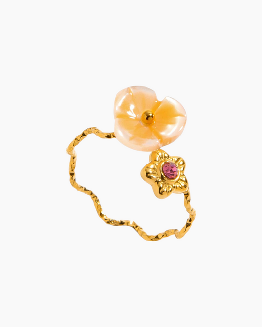 Gold ring with peach-colored flower and pink gemstone on a white background