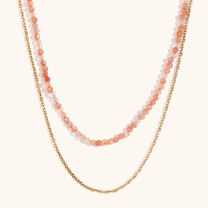 Orange crystal layered necklace with gold chain, displayed against peach backdrop