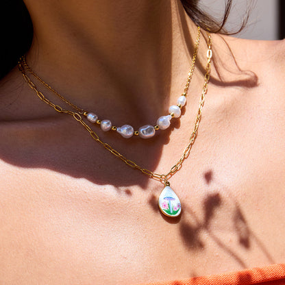 Model wearing gold and pearl layered necklace with floral mushroom enamel charm in orange top
