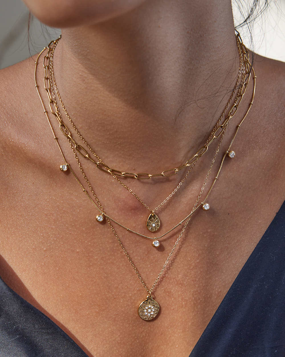 Close-up of a person wearing multiple gold necklaces with pendants.