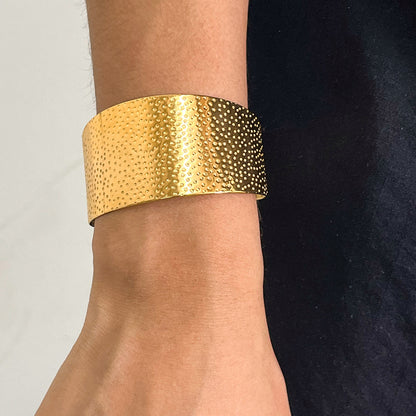 Gold textured cuff bracelet on a wrist with a neutral background