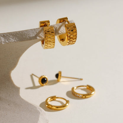 Trio of gold earrings — wide hoops, pave hoops, and gemstone studs — arranged on a glass block.