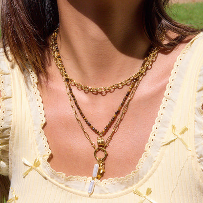 Close-up of woman wearing layered beaded gold necklace with coffee cup charm