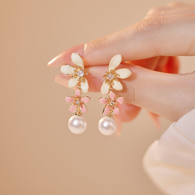Model hand withTimeless pearl and blossom earrings  pink and white flowers, , set in a soft, glamorous scene.