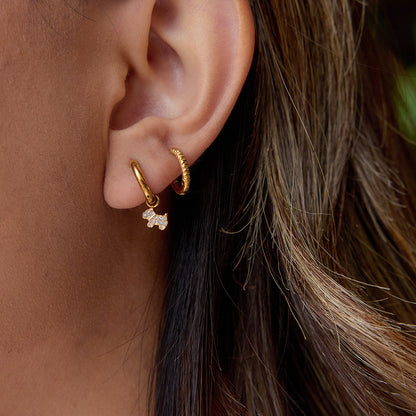 Close-up of gold huggie earrings with sparkly dog charm worn by woman with brown hair