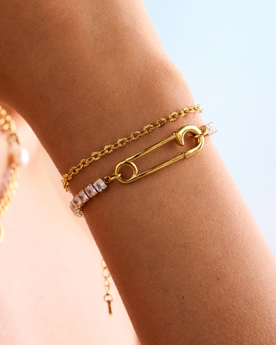 Model's wrist styled with layered gold bracelets including a rhinestone and safety pin design