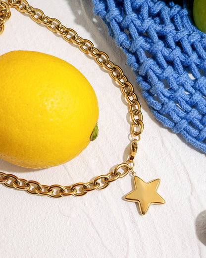 Trendy gold star necklace with blue fabric and berries, lemon accent, modern setup.