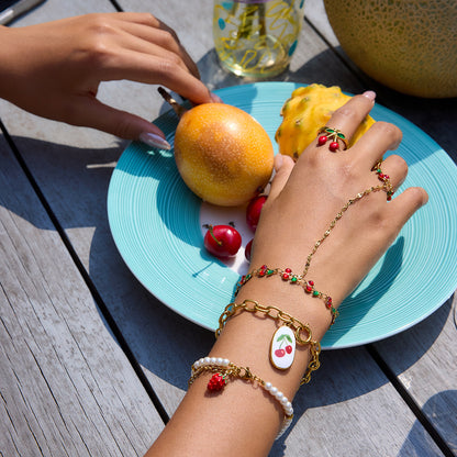 Woman’s hand wearing layered cherry hand chain accessories holding fruit on outdoor table
