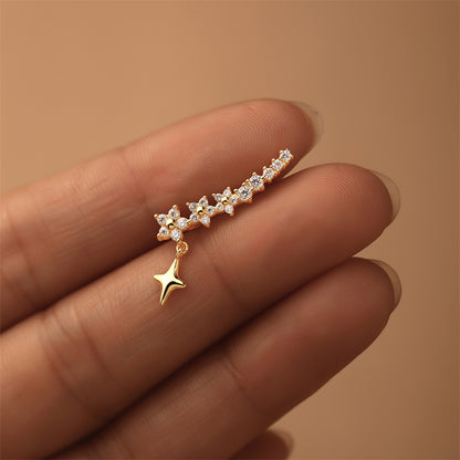 Elegant gold star earrings with chain and crystal accents, held in hand under soft light.