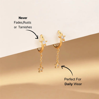 Elegant gold hoop earrings with a sparkling star and dangling charm, featuring cubic zirconia diamonds, on a soft beige background.