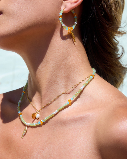 Close-up of a person wearing beaded earrings and necklaces against a light background