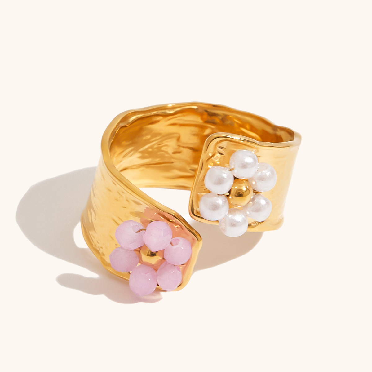 Close-up of a gold open ring with pink and white flower beads placed beside dried petals