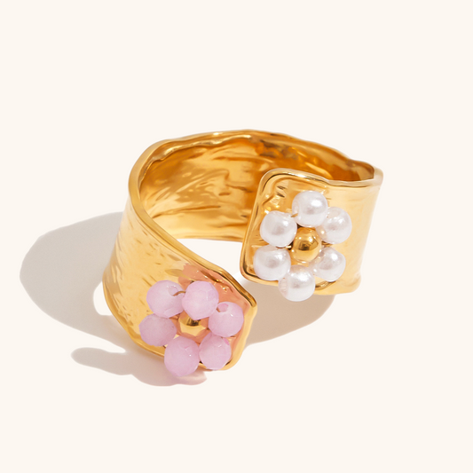 Close-up of a gold open ring with pink and white flower beads placed beside dried petals