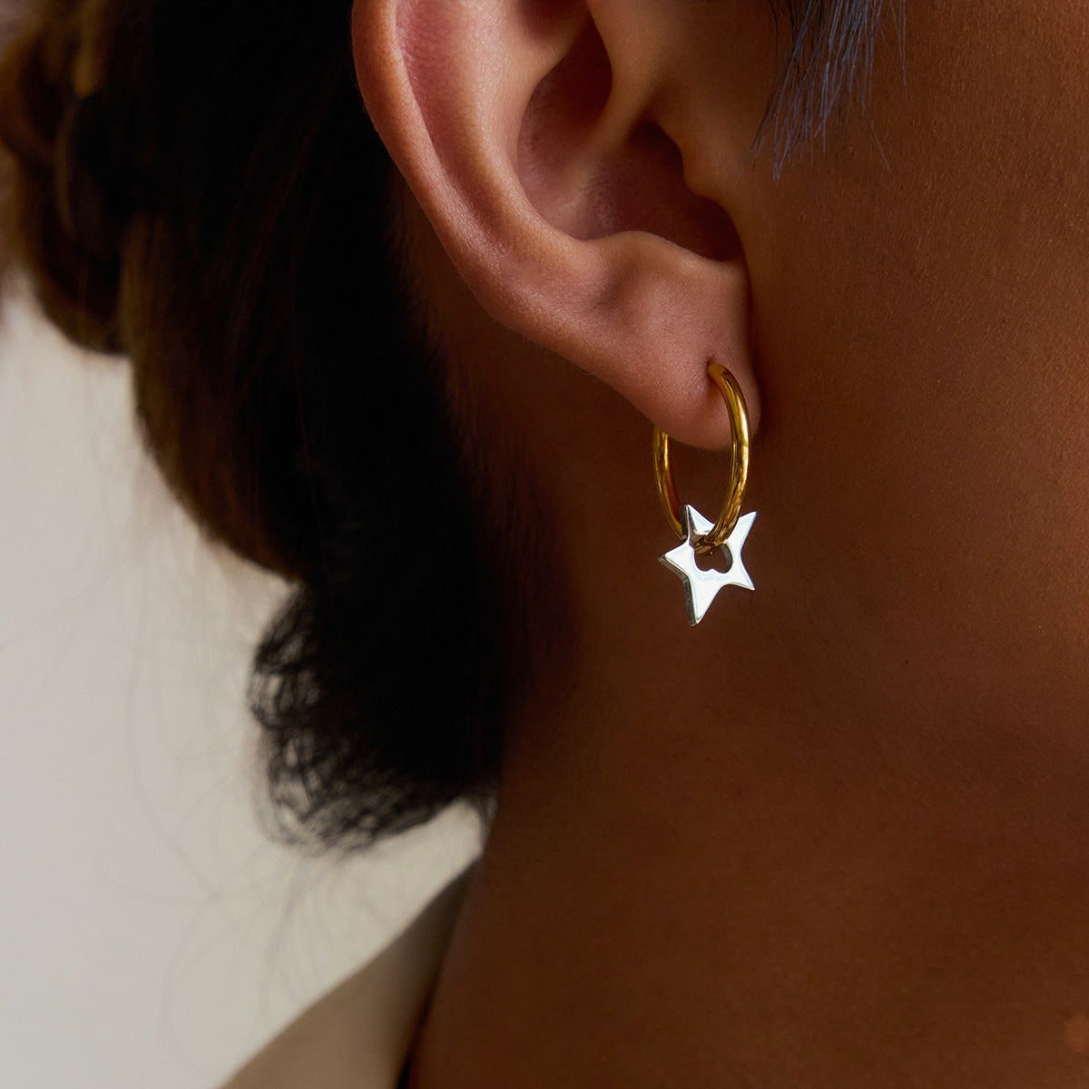 Gold hoop earrings with silver star charms styled on model’s ear