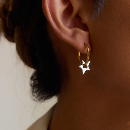 Gold hoop earrings with silver star charms styled on model’s ear