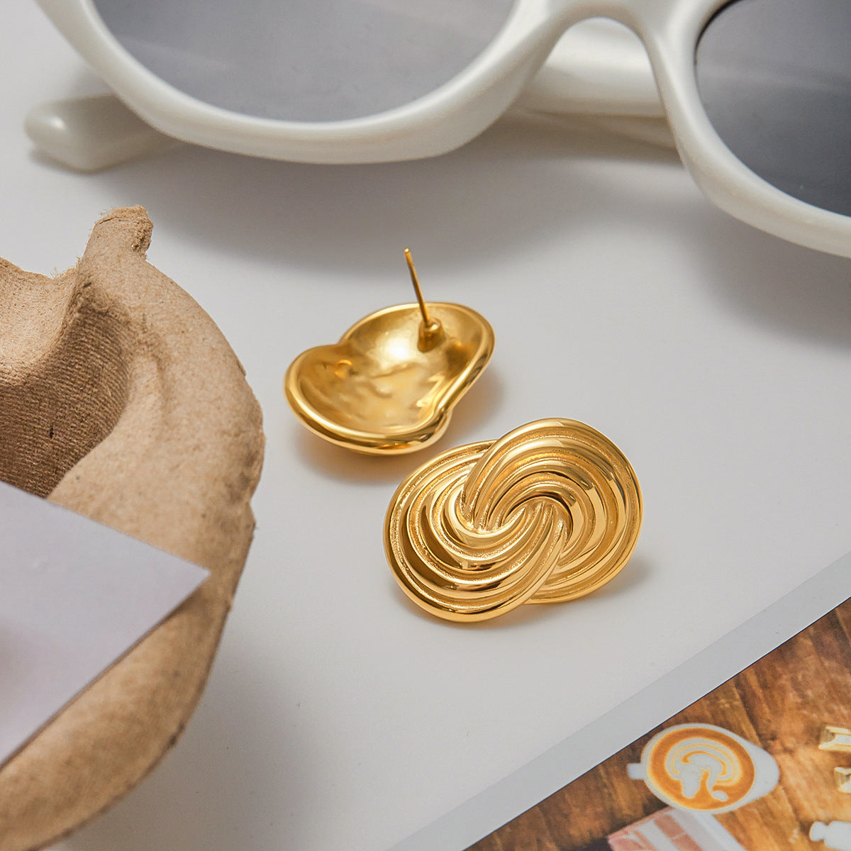 Sculptural gold swirl earrings displayed with summer accessories