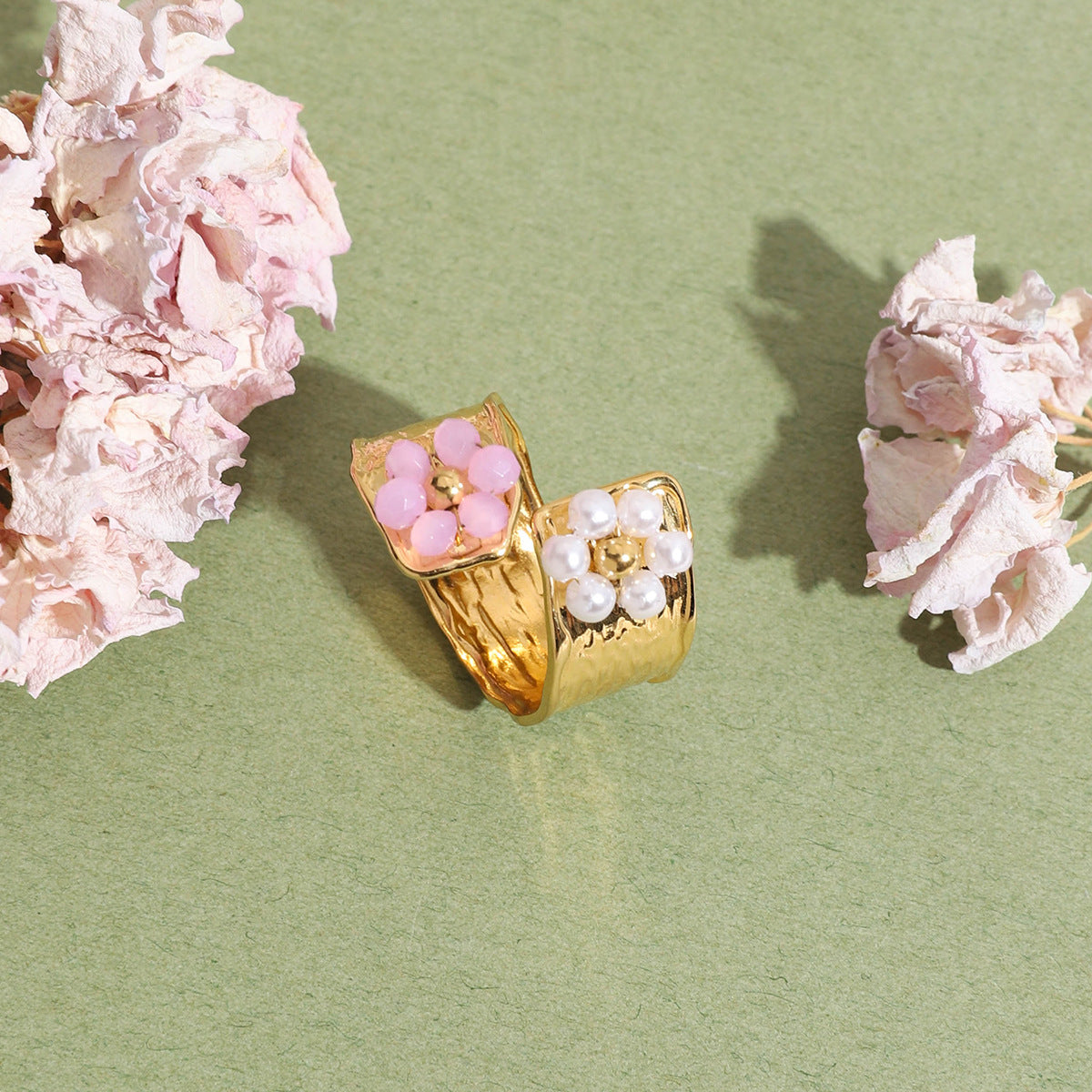 Ring with pearl and pink floral design on green paper background with soft lighting