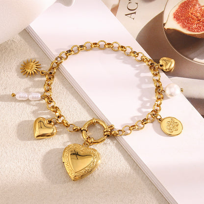 Gold chain bracelet with engraved heart locket and pearl charm on magazine background
