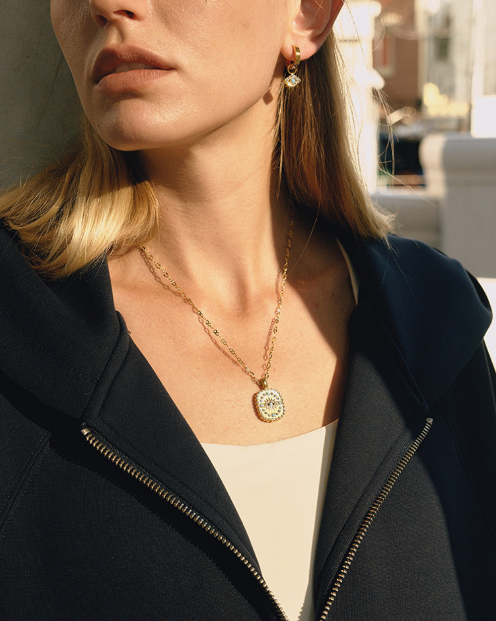 Close-up of vintage inspired gold pendant necklace layered with earrings, highlighting sparkle in sunlight.