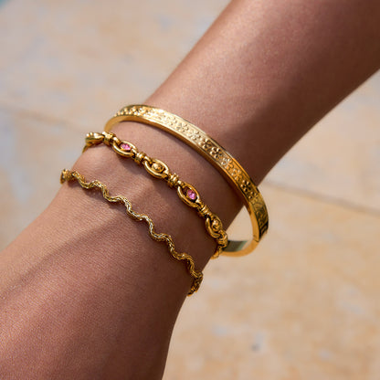 Woman wearing a twisted gold rope bracelet paired with floral and gemstone bangles in bright sunlight