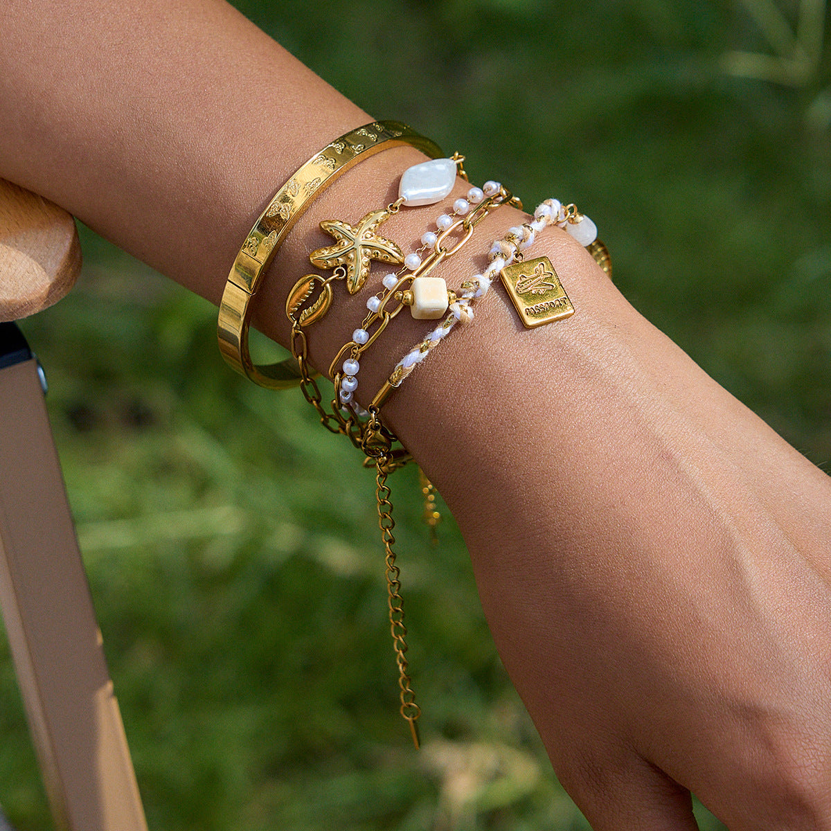 Model wearing gold and white travel charm bracelet in outdoor summer setting
