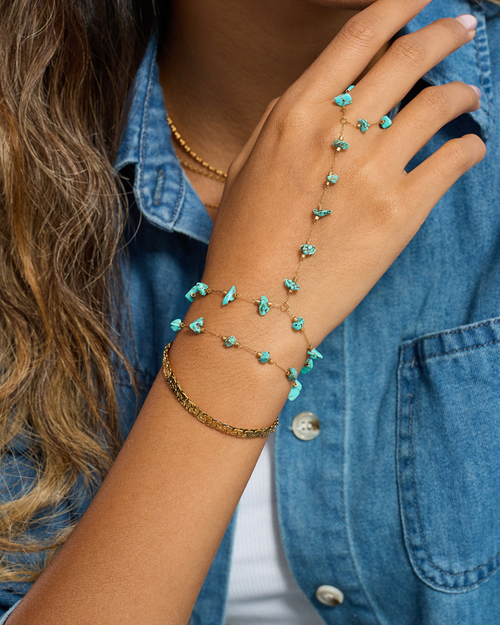 Close-up of a hand wearing a turquoise beaded bracelet with a denim jacket background