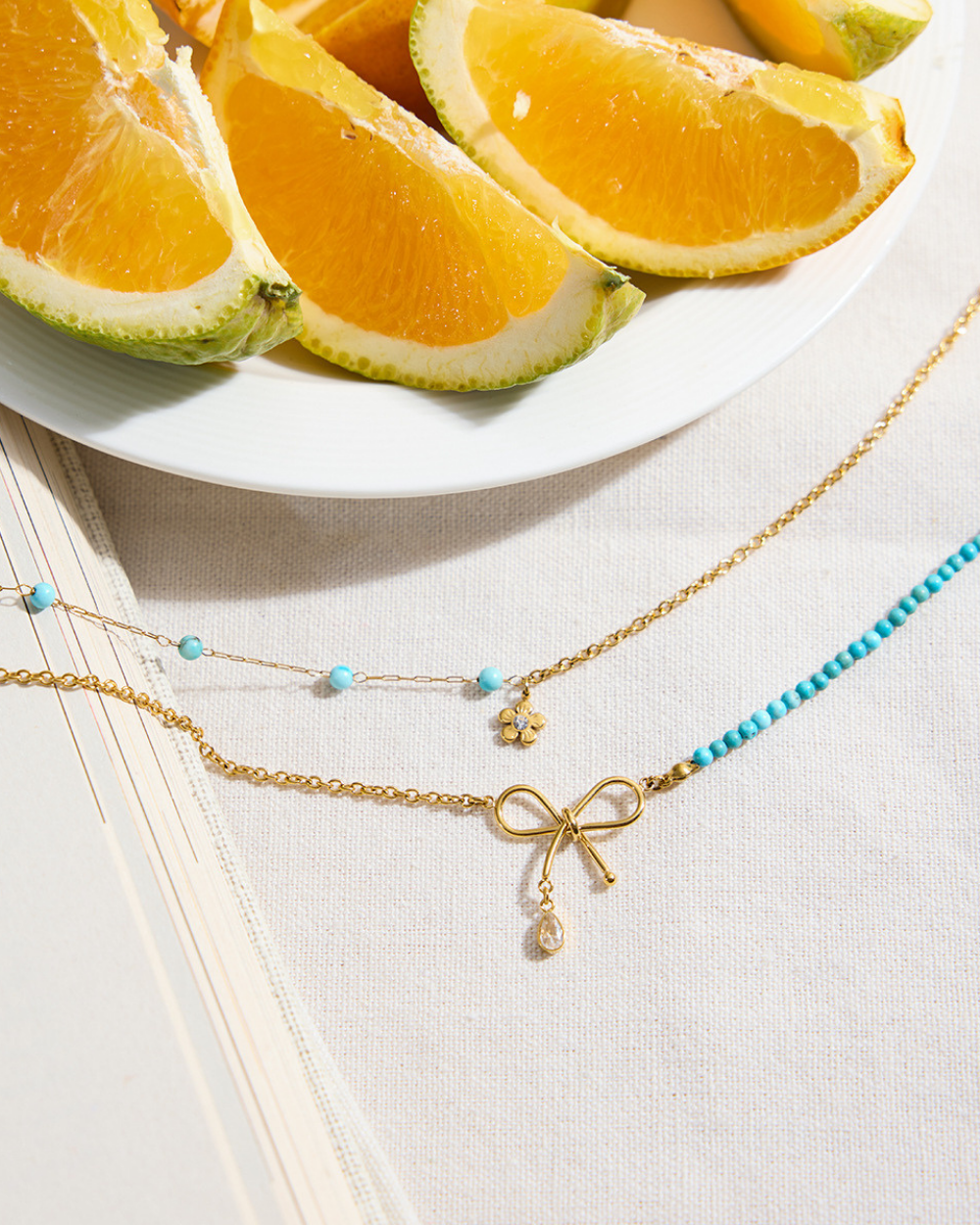Gold necklaces with blue beads on a white surface with orange slices in the background