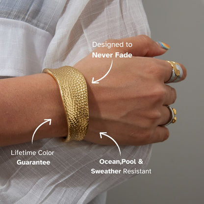 Close-up of a golden cuff bracelet with a hammered texture and reflective polish under bright lighting