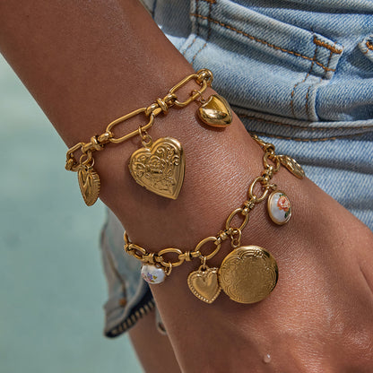 Close-up of gold heart charm bracelet with floral engraving on model wrist