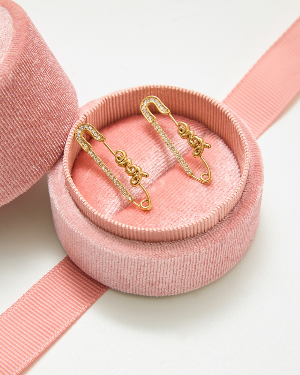 Gold "Love" safety pin earrings displayed in a pink velvet box with a matching ribbon.