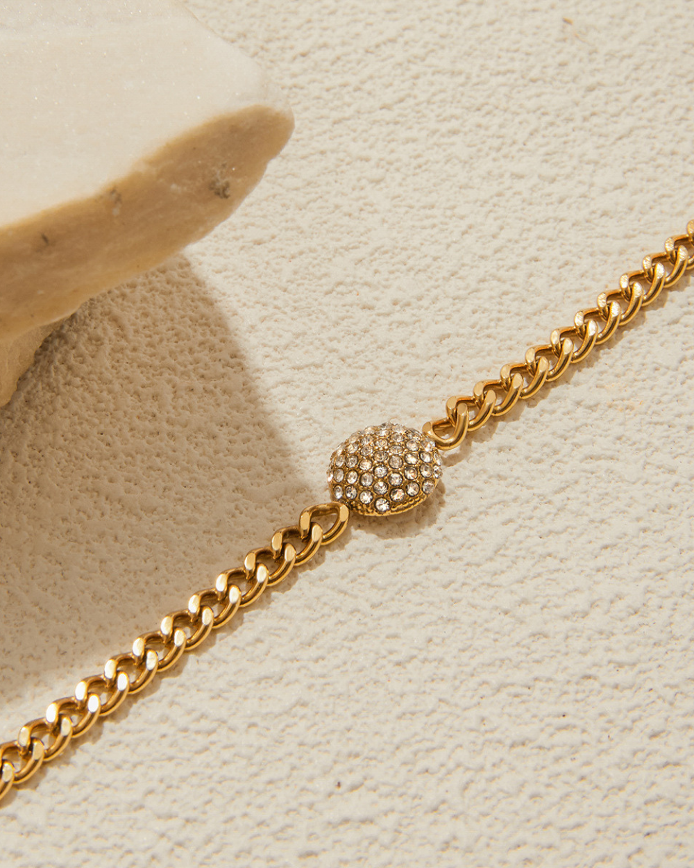 Gold chain bracelet with a decorative clasp on a textured beige surface