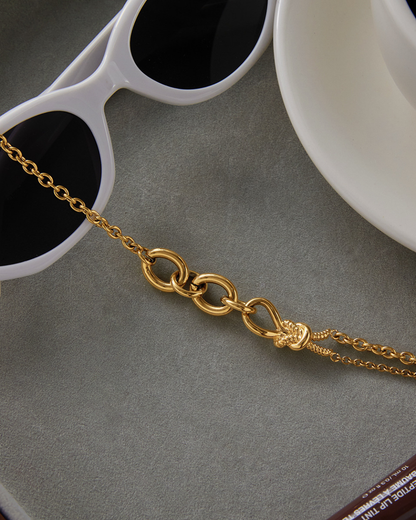 Gold chain necklace on a gray surface with sunglasses and a white dish in the background.