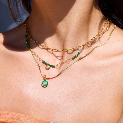 Model wearing layered gold and green necklaces with beachwear