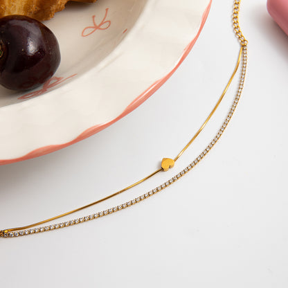 Gold necklace with a heart pendant on a white surface with a cherry and plate in the background.