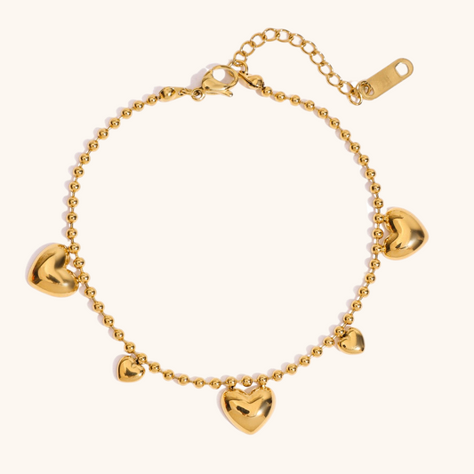flat lay of gold heart bracelet with beaded chain on cream background