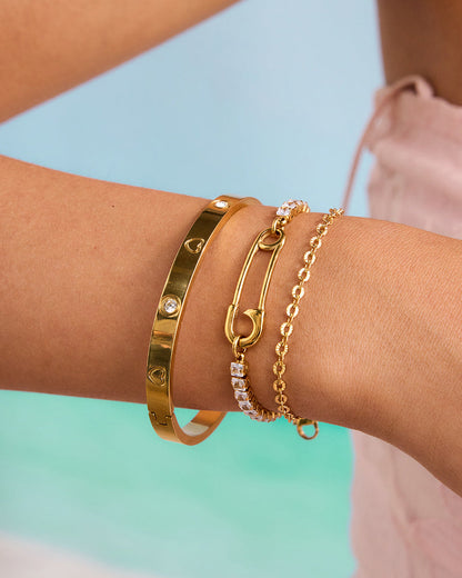 Woman wearing three gold bracelets, including a rhinestone safety pin chain, styled for summer