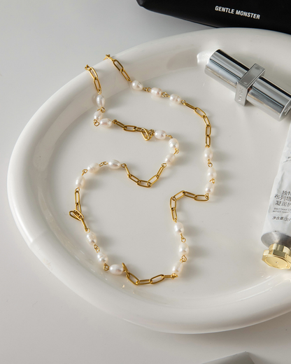 Pearl and gold chain necklace on a white plate with a bottle of skincare product.