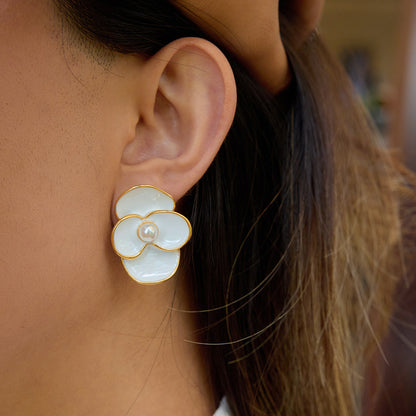 Gold-edged petal earrings placed on white surface next to sunglasses