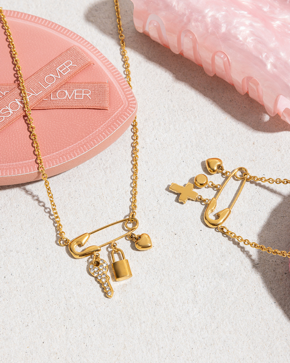 Gold necklaces with charms on a light surface with 'LOVER' branding.