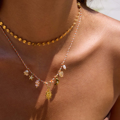 Model wearing gold coin choker necklace layered with charm strand on sun-kissed skin