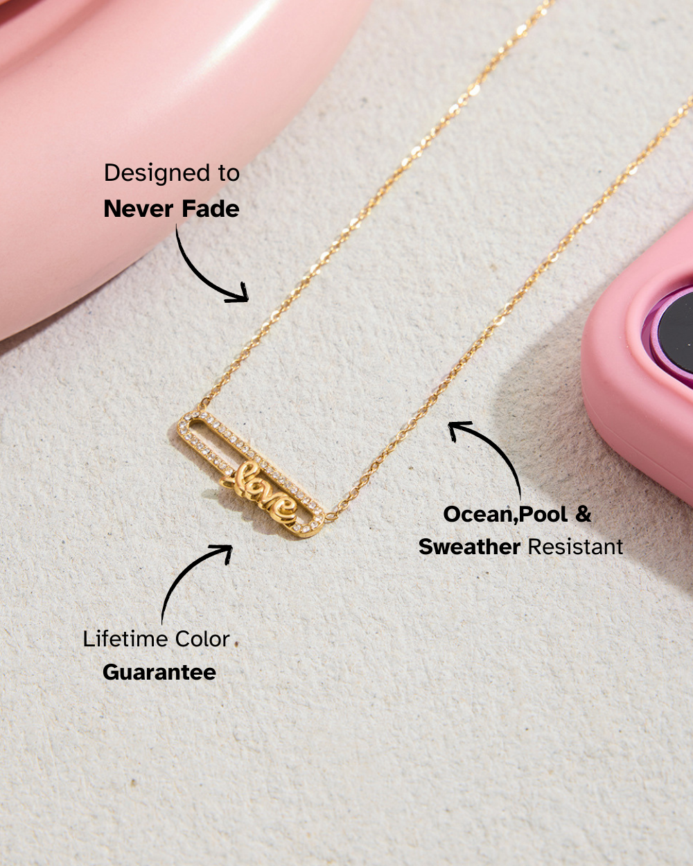 Lifestyle photo of M&F Jewelry gold LOVE necklace placed on beige surface with pink accessories, highlighting waterproof and never fade features.