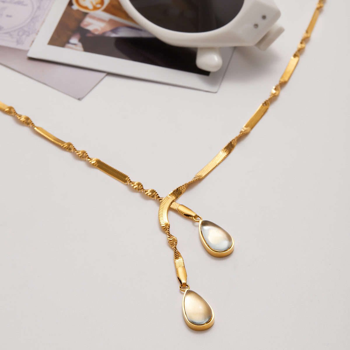 Gold necklace with teardrop pendants on a light gray surface