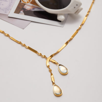 Gold necklace with teardrop pendants on a light gray surface