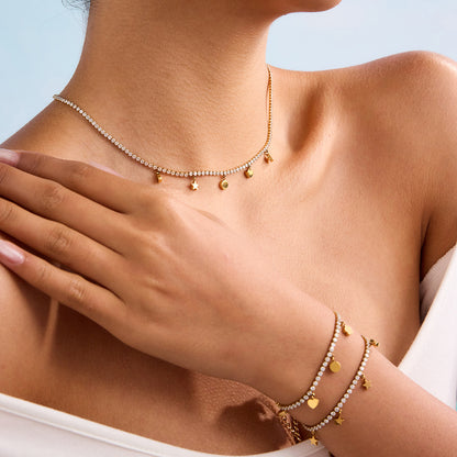 Model layering two gold charm bracelets on wrist with matching necklace