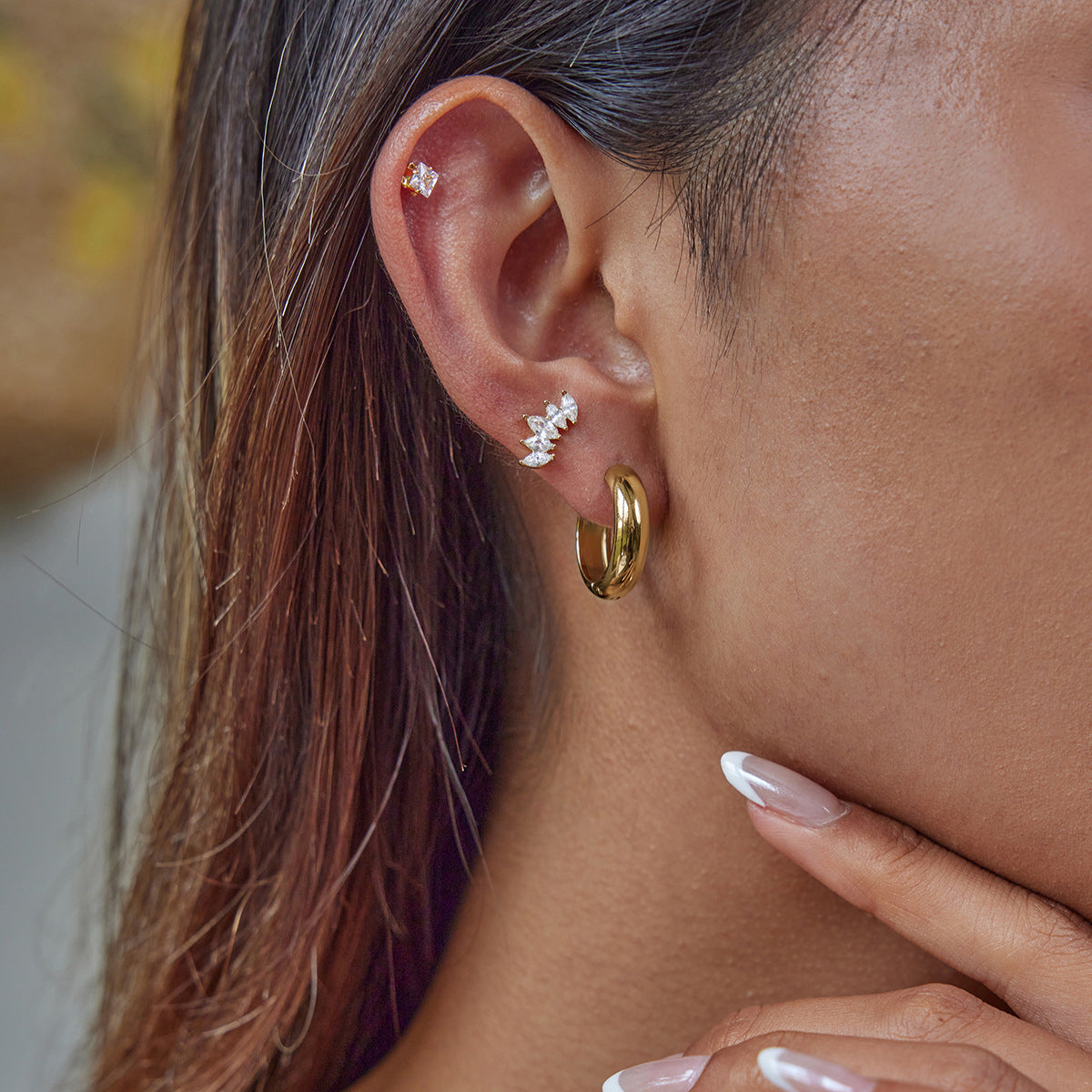 Model wearing thick gold huggie hoops with stacked ear piercings